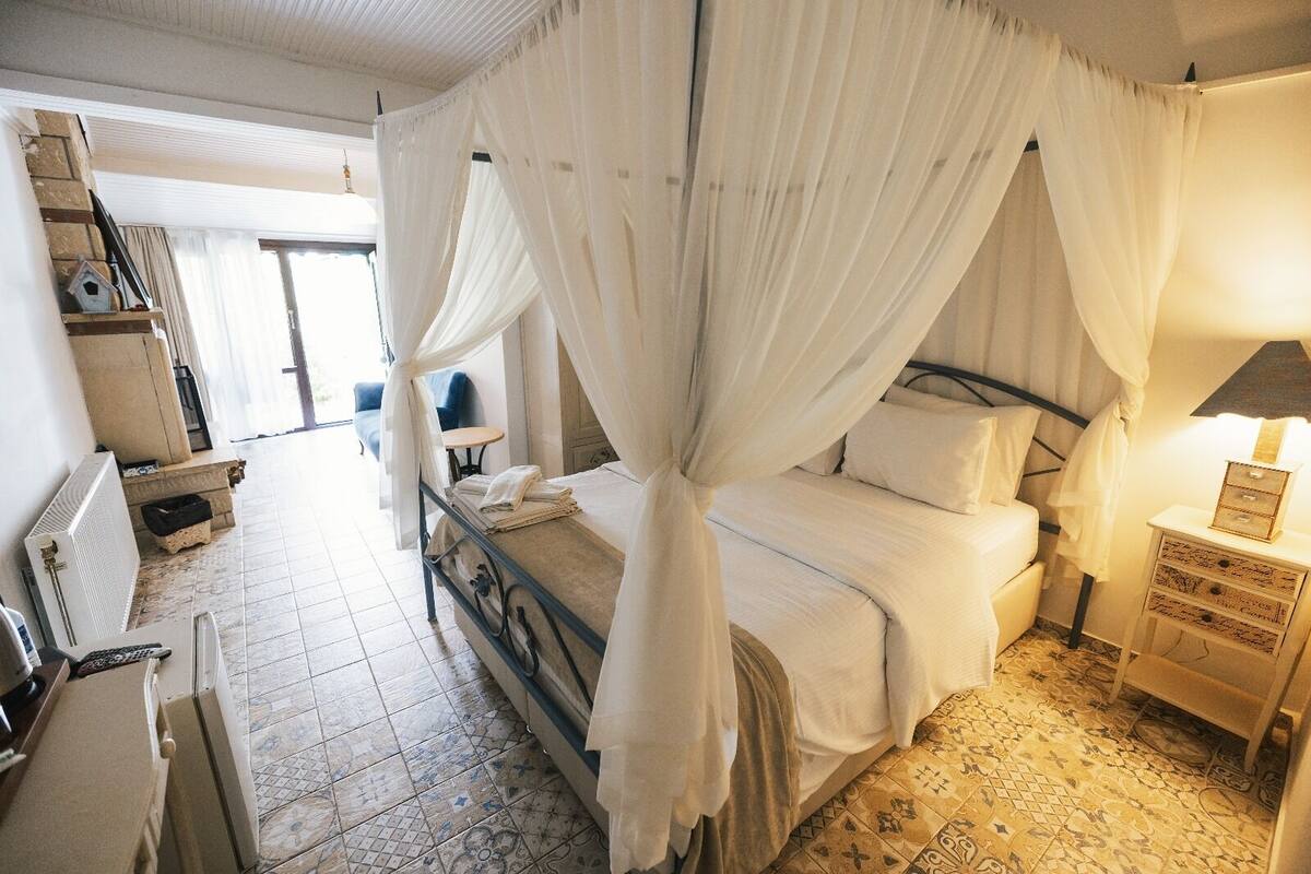 Une chambre avec un lit sous un dais, une table de chevet avec une lampe, une chaise et une petite table avec une autre chaise.