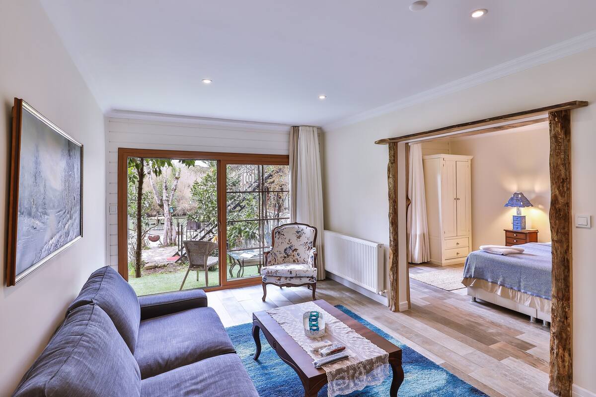 Un salon spacieux comprenant un canapé, une table basse et un fauteuil. Une grande fenêtre offre une vue sur l’extérieur.