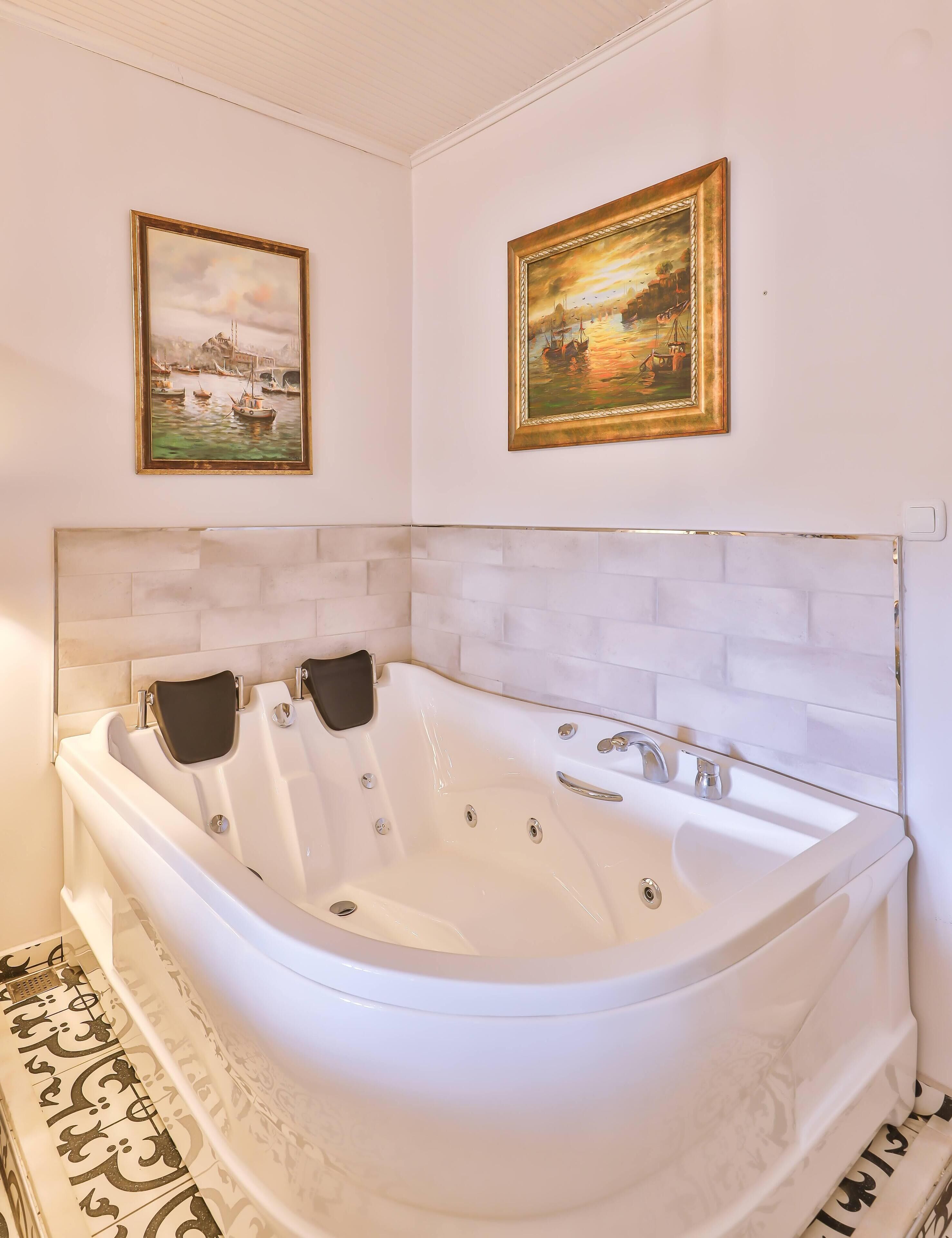 Um banheiro moderno com uma banheira independente, paredes com azulejos brancos e duas pinturas emolduradas acima da banheira.