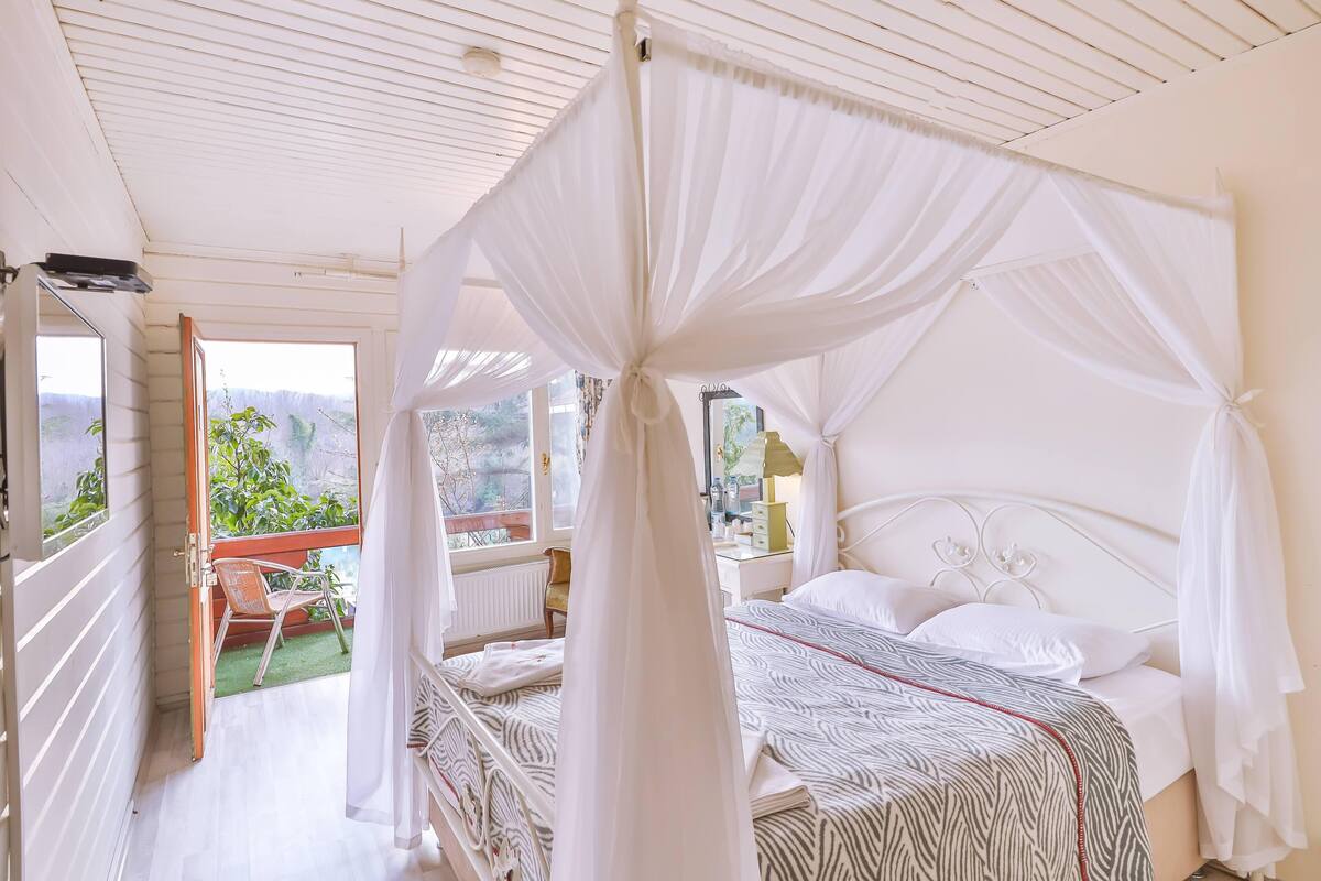 Une chambre à coucher avec un lit à baldaquin, une vue sur l’extérieur et un petit balcon avec une chaise.
