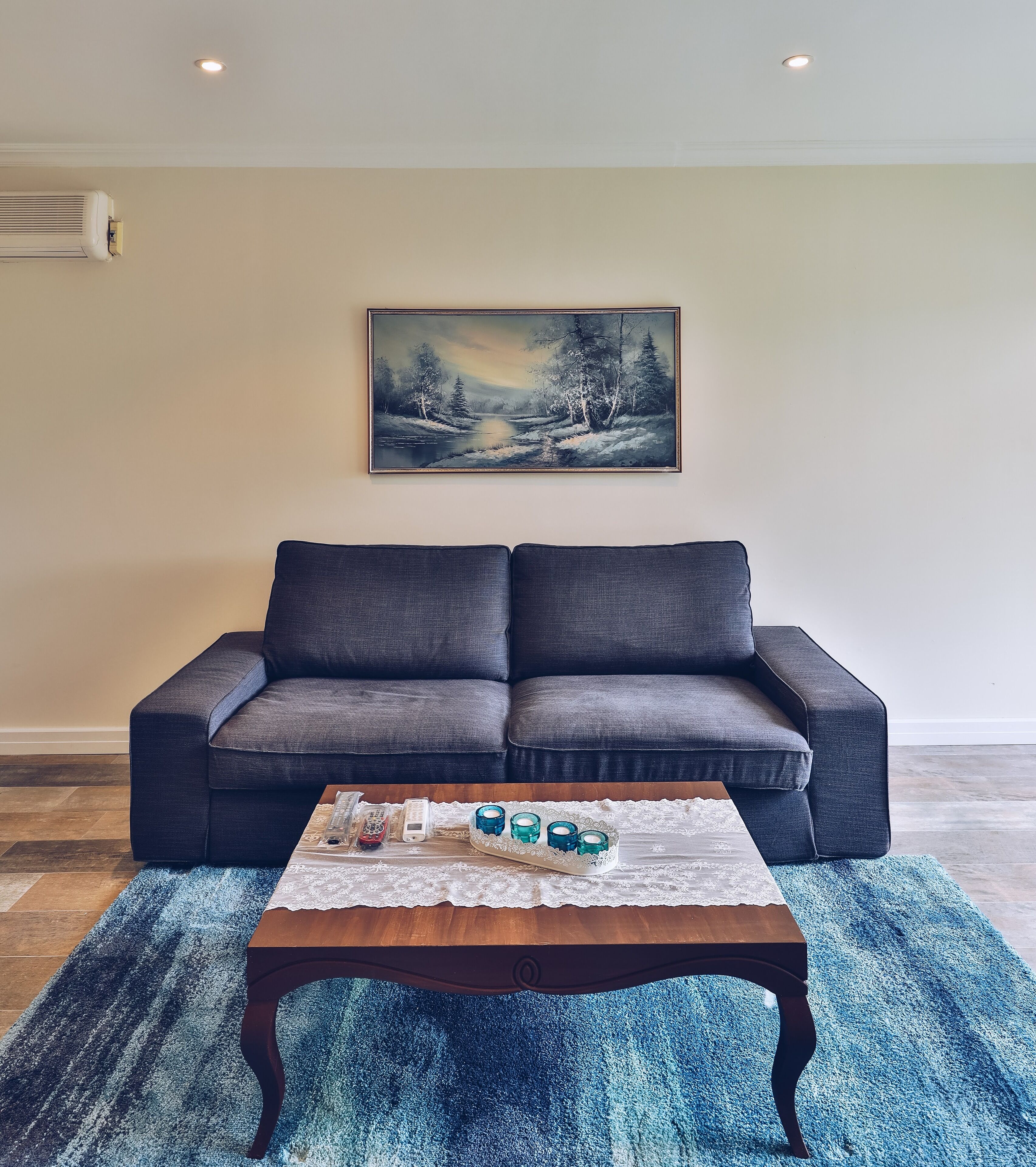 A living room with a dark grey sofa, a wooden coffee table with decorative items, and a framed painting of a winter landscape on the wall.