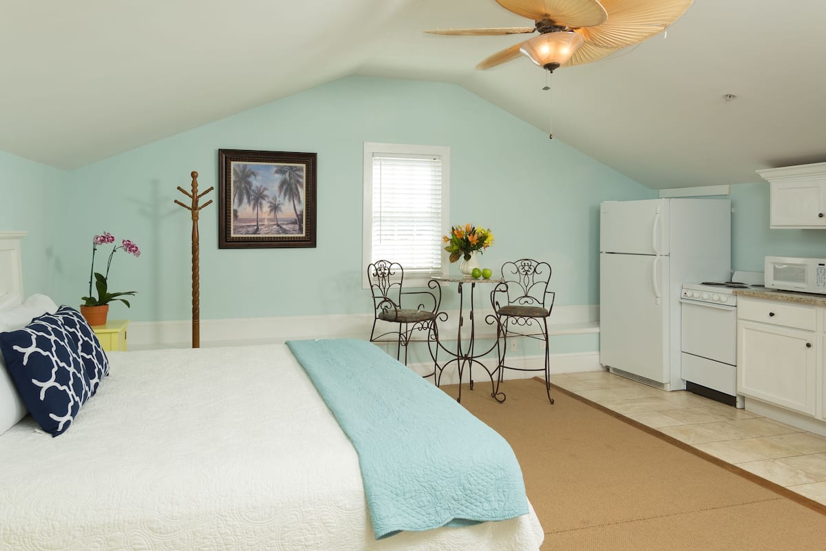 A bedroom with a bed, a desk, and a kitchenette.