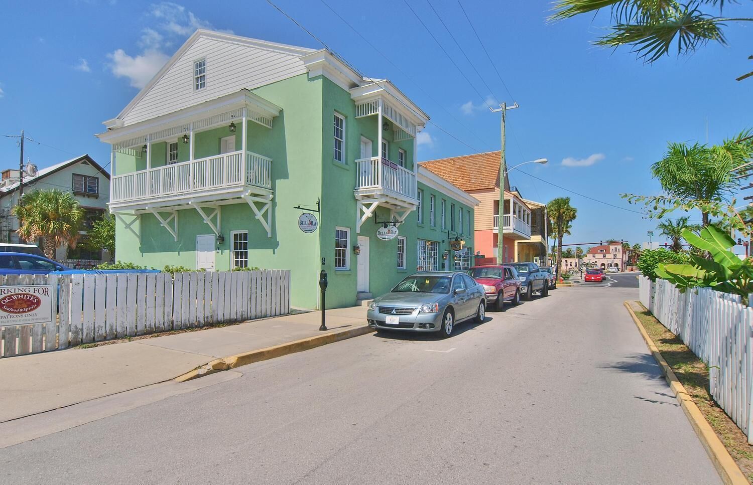 A street view with a green building featuring a balcony and a sign that reads "Bell Bay".