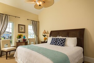 A hotel room with a large bed, a chair, a desk with a lamp, and a window with curtains.