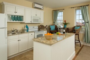 A kitchen with white cabinets, a granite countertop, and a central island with a bowl of fruit.