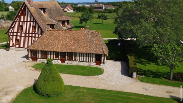 Une maison traditionnelle à colombages, avec des fondations en pierre et un toit en tuiles, entourée d’une pelouse bien entretenue et d’un petit arbre.