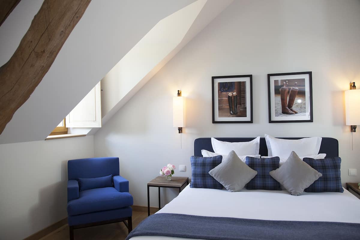 Une chambre à coucher avec un lit, un fauteuil bleu et deux tableaux encadrés accrochés au mur.