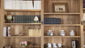 A wooden bookshelf with books, a globe, a lamp, a framed picture, jars, cups, a bird figurine, and a vase with flowers.