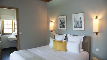 A hotel room with a large bed, a bedside table, a nightstand, a window with a view, and a bathroom with a sink and mirror.