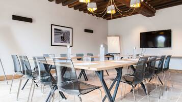 A conference room with a large table, clear chairs, a mounted TV, and a wooden ceiling.