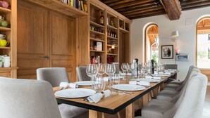 Une longue table à manger, dressée avec de l’argenterie blanche, des verres et des couverts, et entourée de chaises rembourrées.