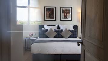 A bedroom with a large bed, a nightstand with a vase of flowers, and two framed pictures on the wall.