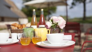 Une table dressée avec des tasses, une théière et des bouteilles, et en arrière-plan, un panier de croissants et un vase de fleurs.