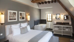 Une chambre avec un grand lit, une salle de bain avec une baignoire et un meuble-lavabo avec deux vasques.