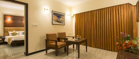 Habitación de hotel con cama, dos sillones, una mesita con frutero, un cuadro en la pared y una cortina.