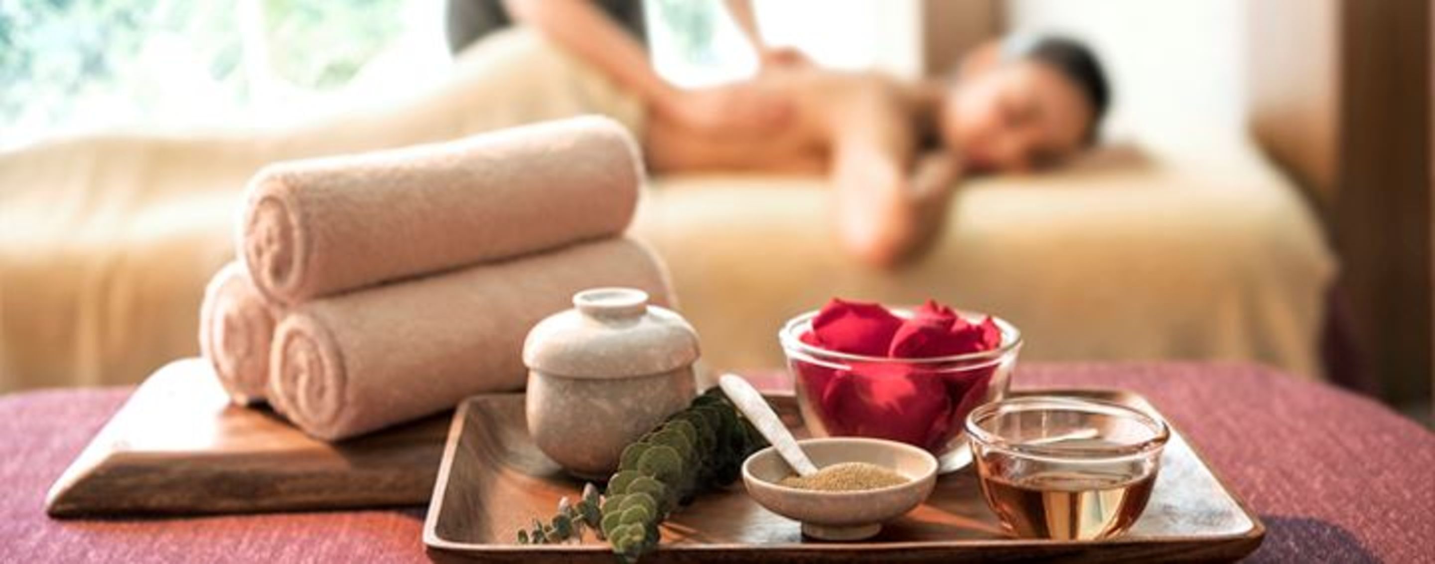 A spa setting with a massage table, towels, a tray with essential oils, and a rose.