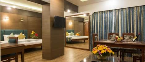 A hotel room with a bed, a desk, a chair, a table, and a TV.