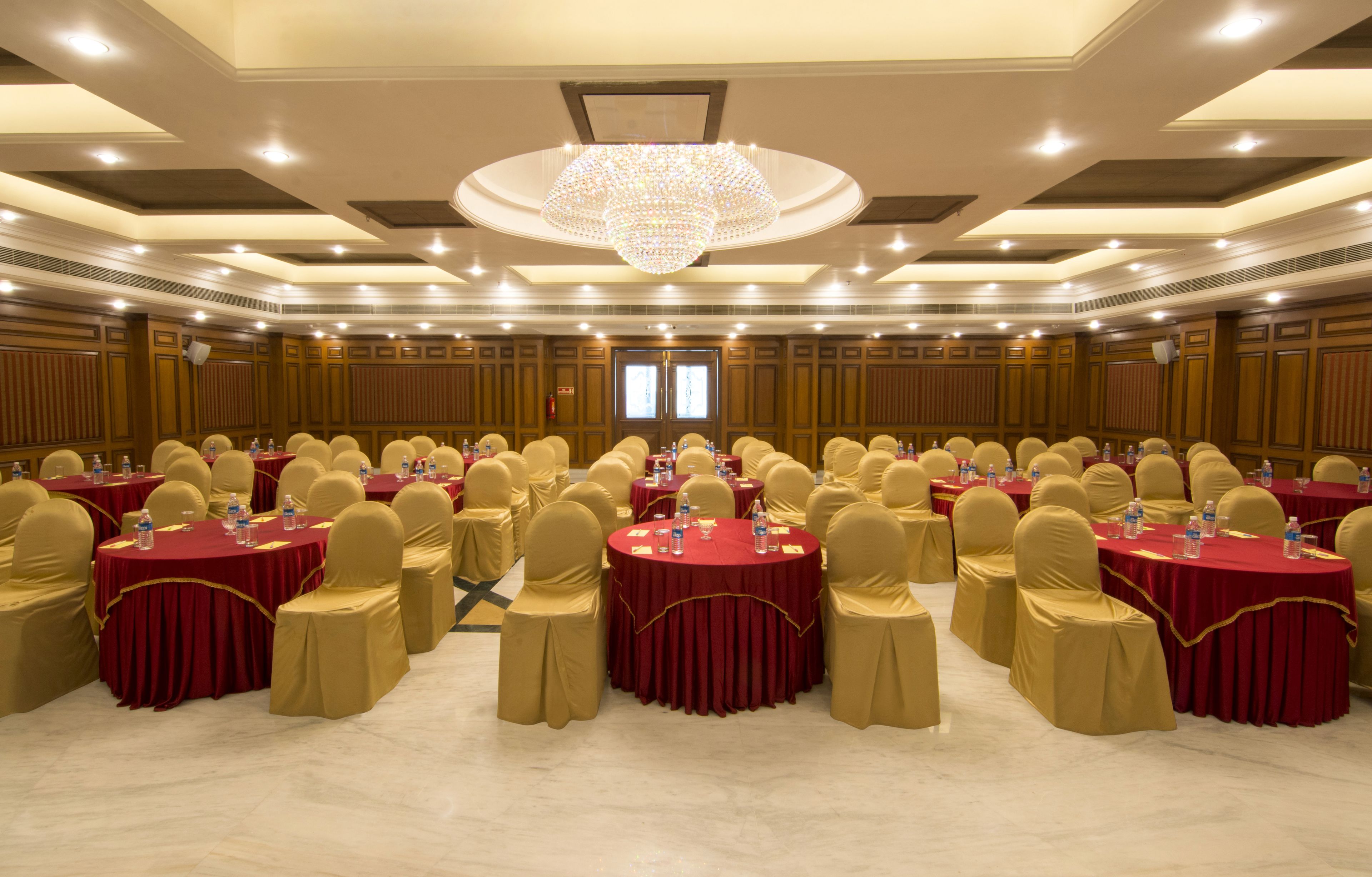 Une grande salle de conférence équipée de tables rondes, de chaises et d’un lustre.