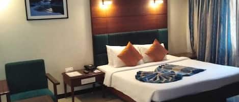 Une chambre d’hôtel avec un lit, un bureau, une chaise, une table de chevet, un tableau au mur et un rideau.