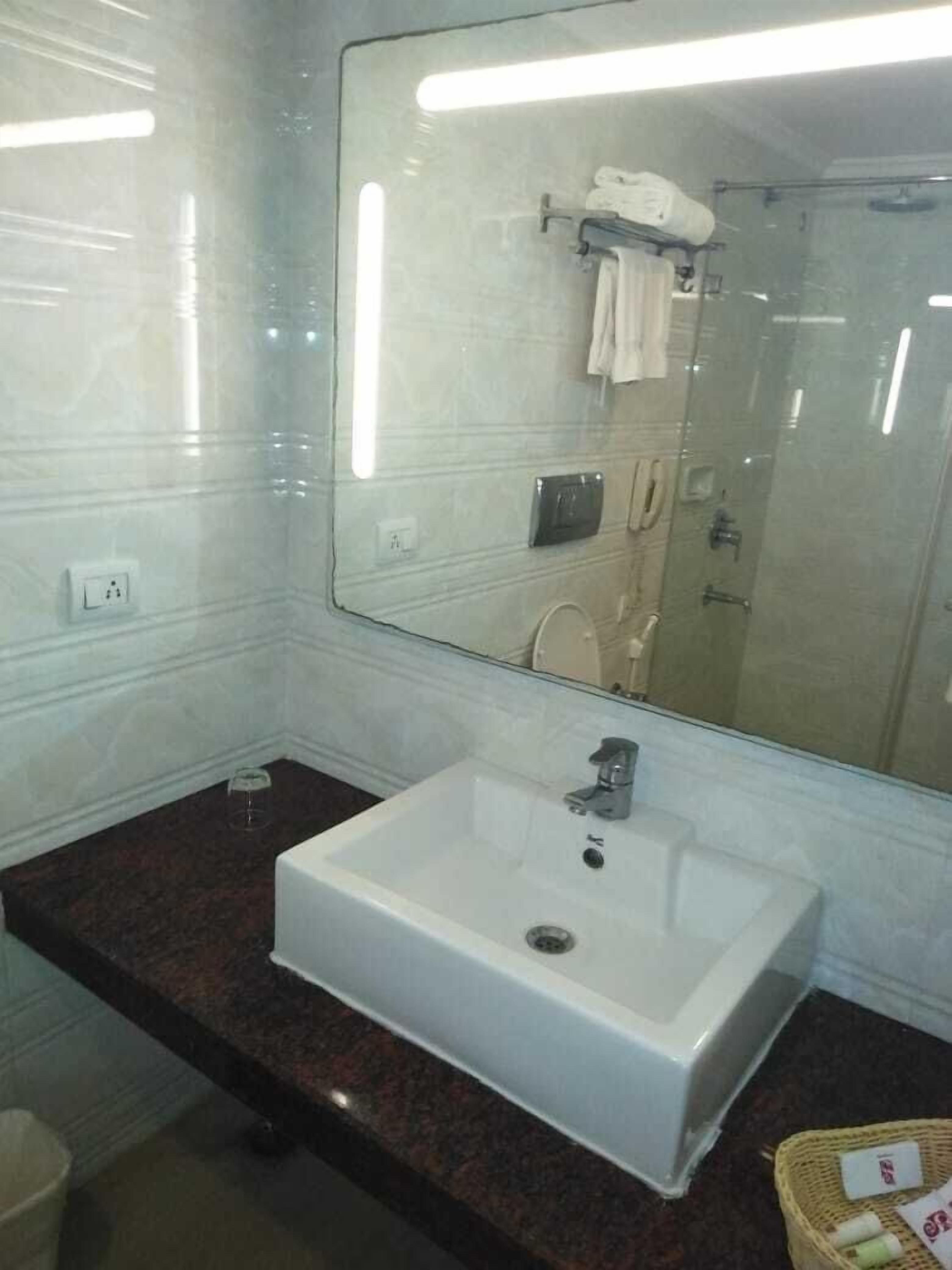 Un baño con un lavamanos blanco, un espejo grande y una cabina de ducha de vidrio.