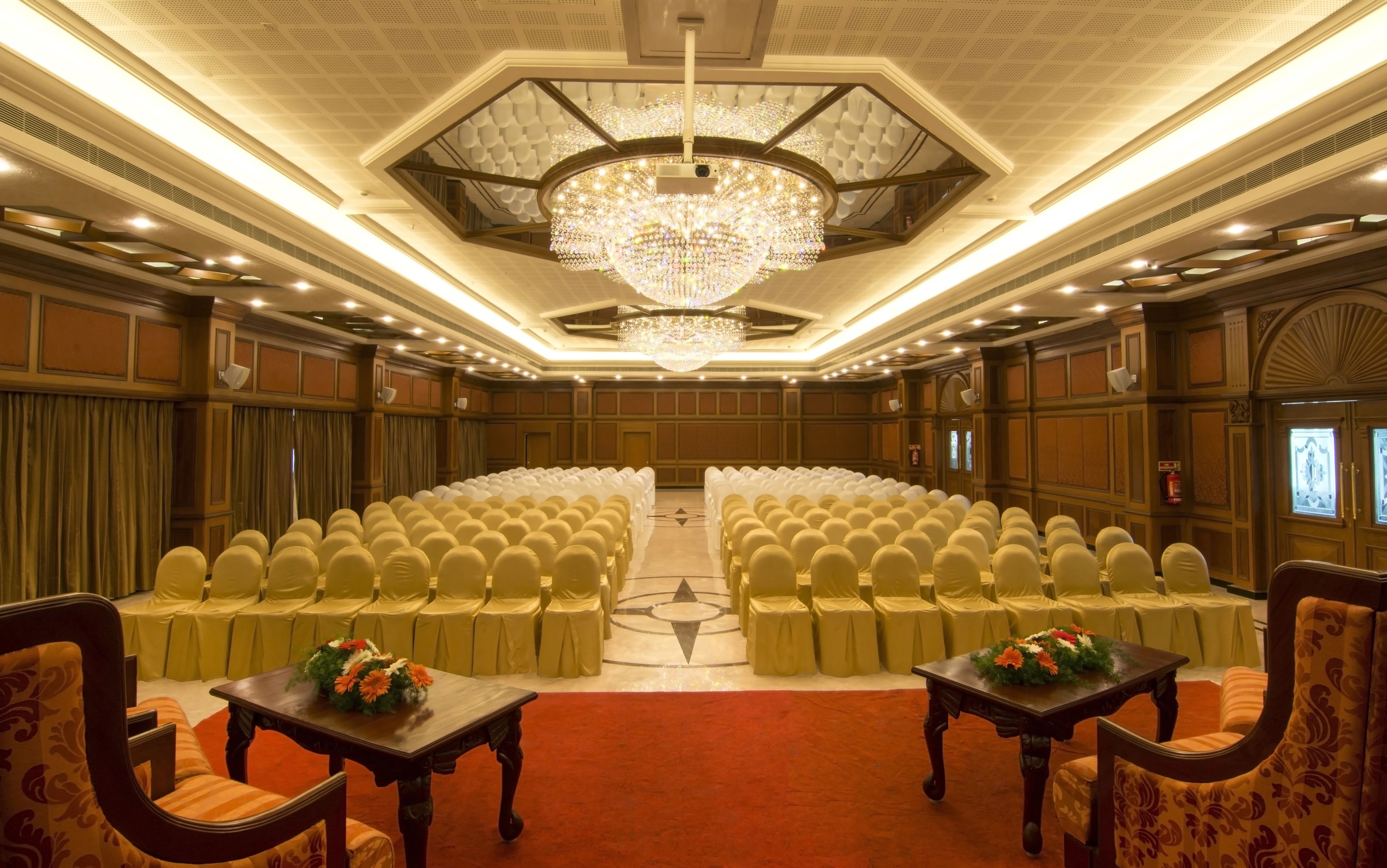 A conference room with rows of chairs, a large chandelier, and tables with floral centerpieces.