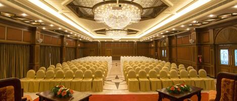 A conference room with rows of chairs, a large chandelier, and tables with floral centerpieces.