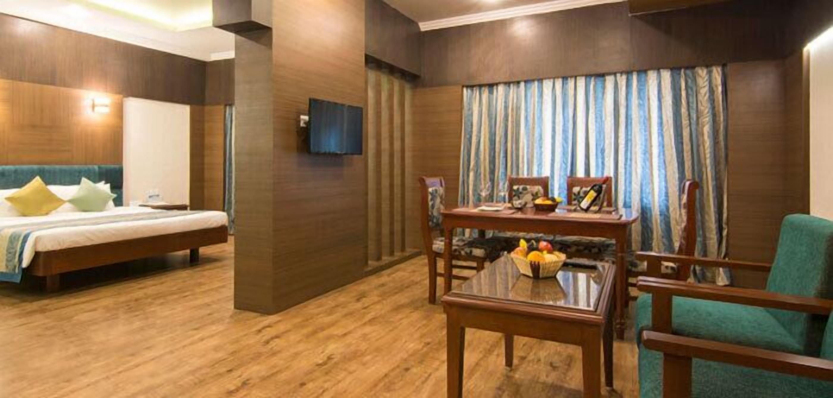 A hotel room with a bed, a dining table with chairs, a TV, and a window with curtains.