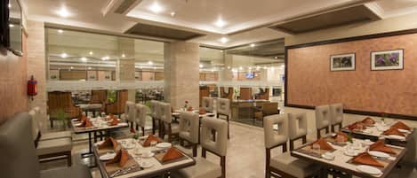 Un restaurant spacieux, doté de nombreuses tables et chaises, d’un extincteur fixé au mur et de tableaux encadrés qui décorent les murs.