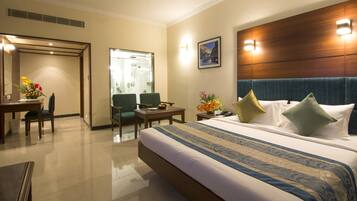 A hotel room with a large bed, a desk with a chair, a small table, and a mirror.