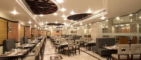 Um restaurante amplo com várias mesas e cadeiras, um design moderno no teto e um interior limpo e bem iluminado.