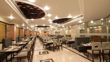 A spacious restaurant with multiple dining tables and chairs, a modern ceiling design, and a clean, well-lit interior.