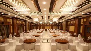 A banquet hall with round tables, white chairs, and chandeliers. - Shenbaga Hotel and Convention Centre (Puducherry)