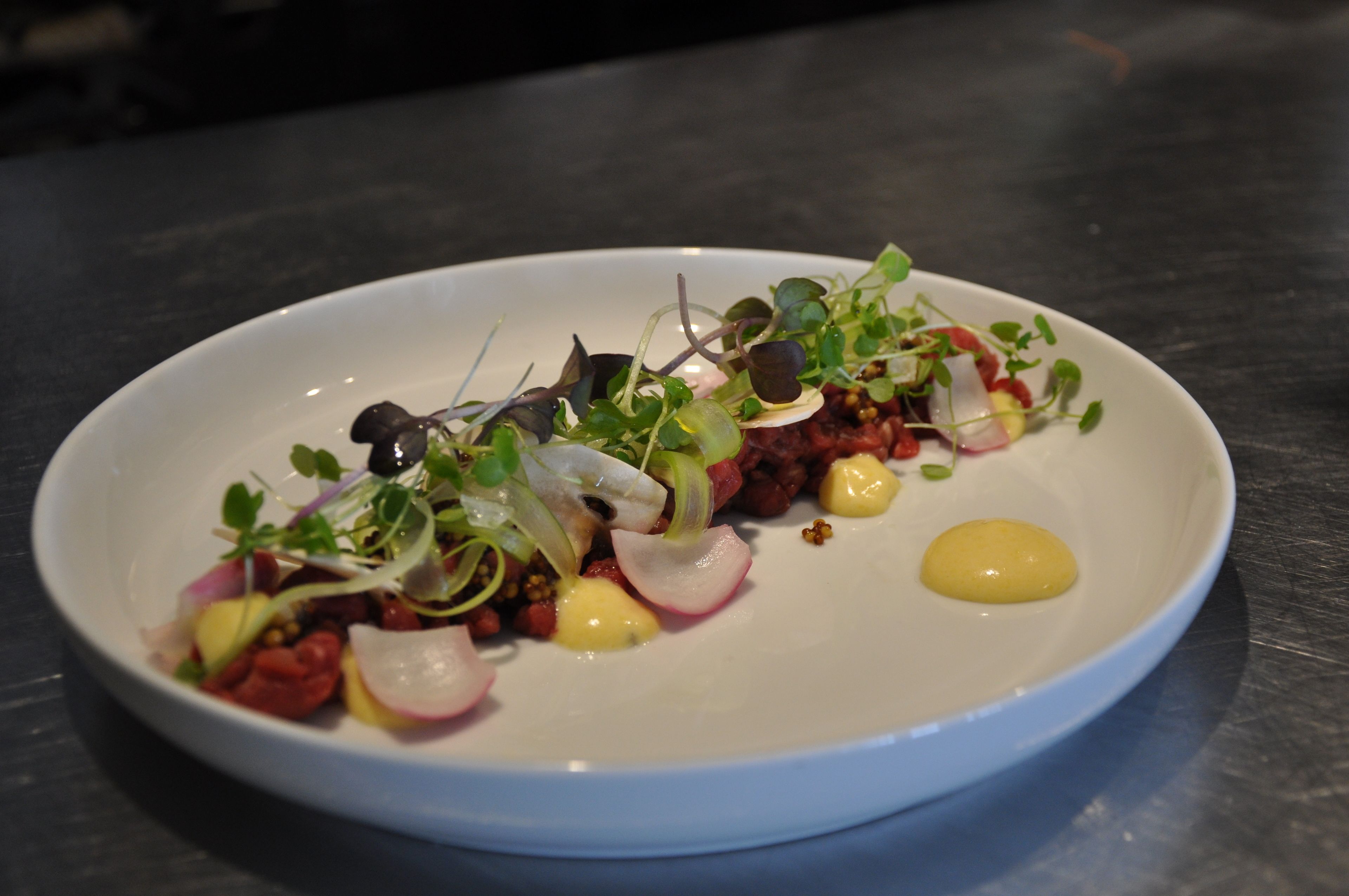 A white plate with a variety of food items including vegetables and possibly meat, arranged on a dark surface.