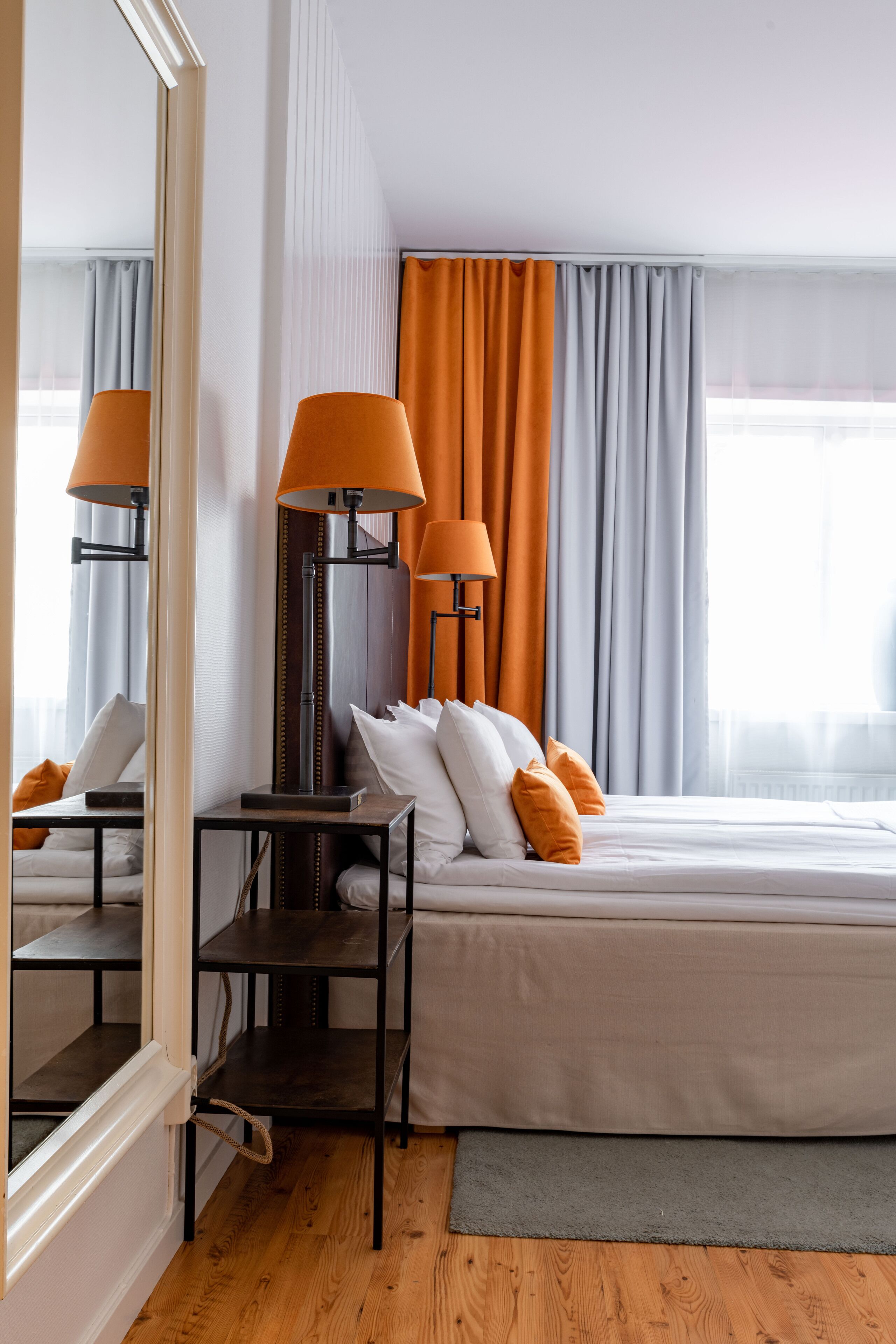Habitación de hotel con cama, dos lámparas, un espejo y ventana con cortinas.