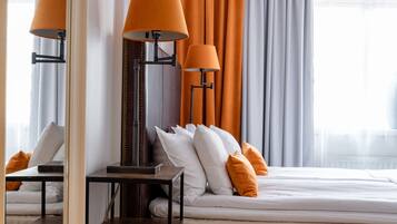 Habitación de hotel con cama, dos lámparas, un espejo y ventana con cortinas.