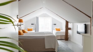 Un dormitorio con techo inclinado, dos camas, un televisor y una ventana con cortinas.