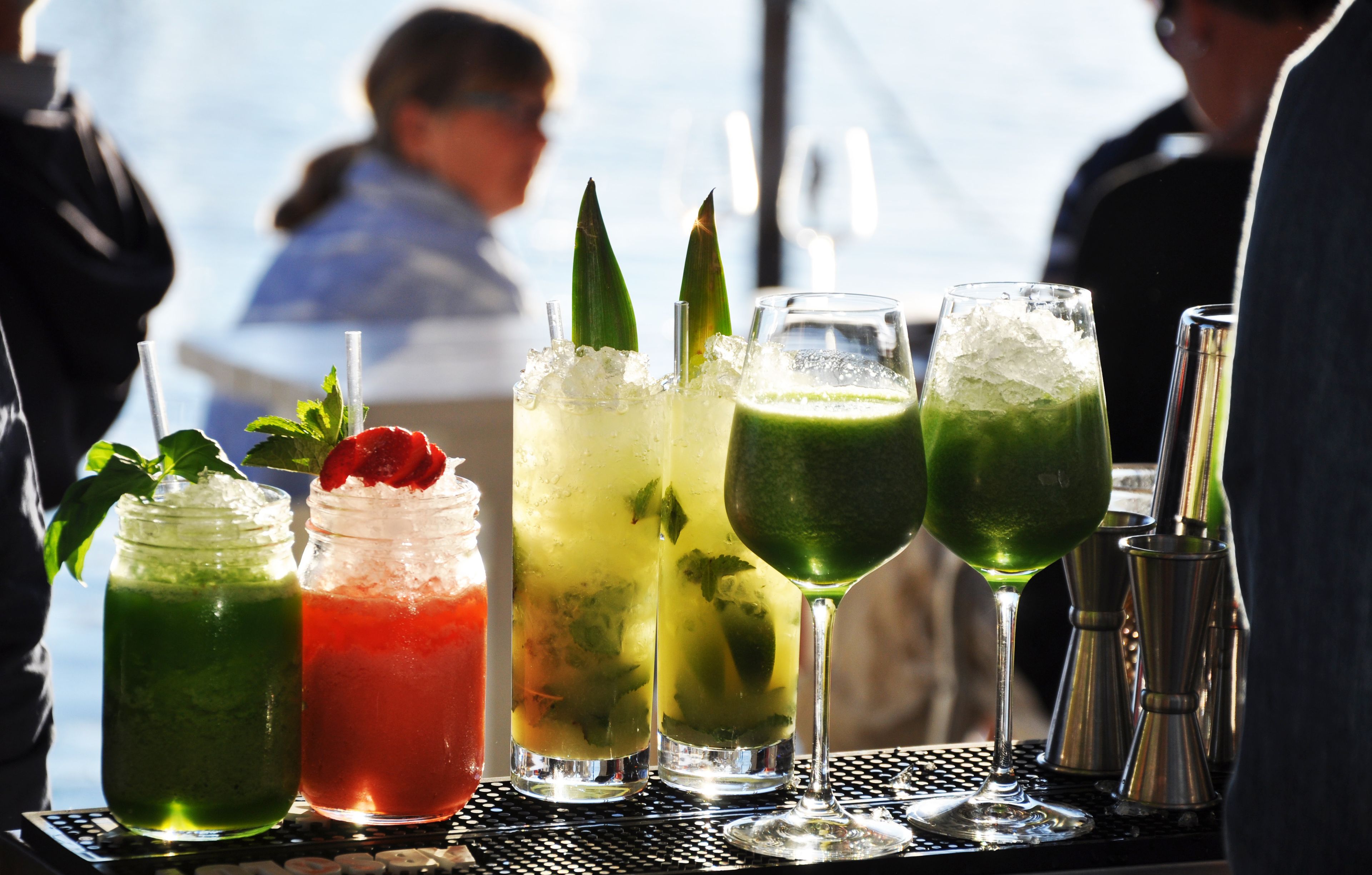 A bar with various drinks, including a green cocktail and a red drink with a strawberry garnish.
