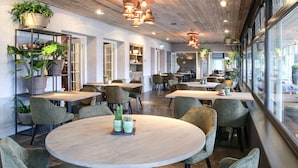 Een modern restaurantinterieur met houten plafonds, ronde tafels en groene stoelen.