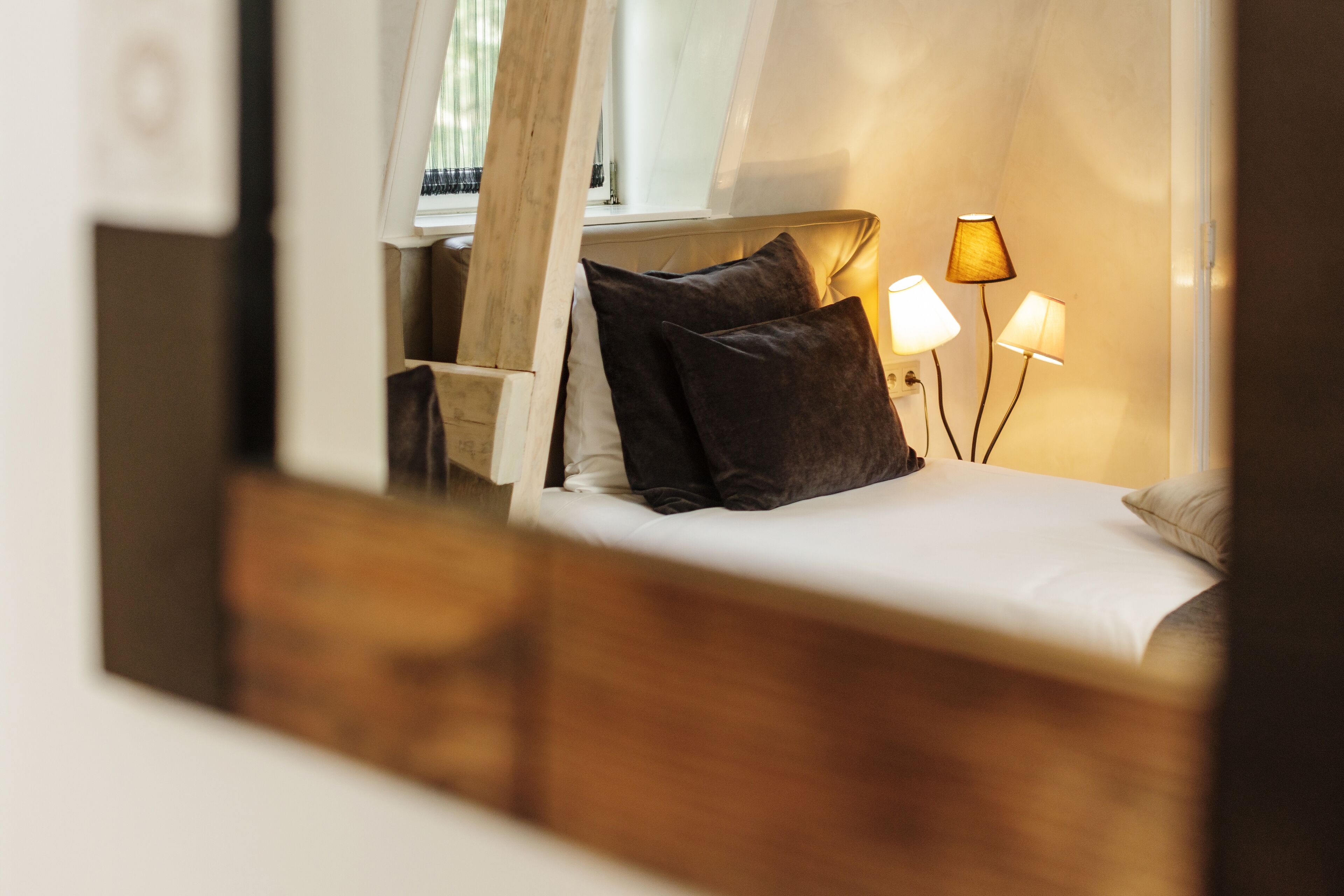 A bedroom with a wooden headboard, a bed with white bedding, two bedside lamps, and a window with curtains.