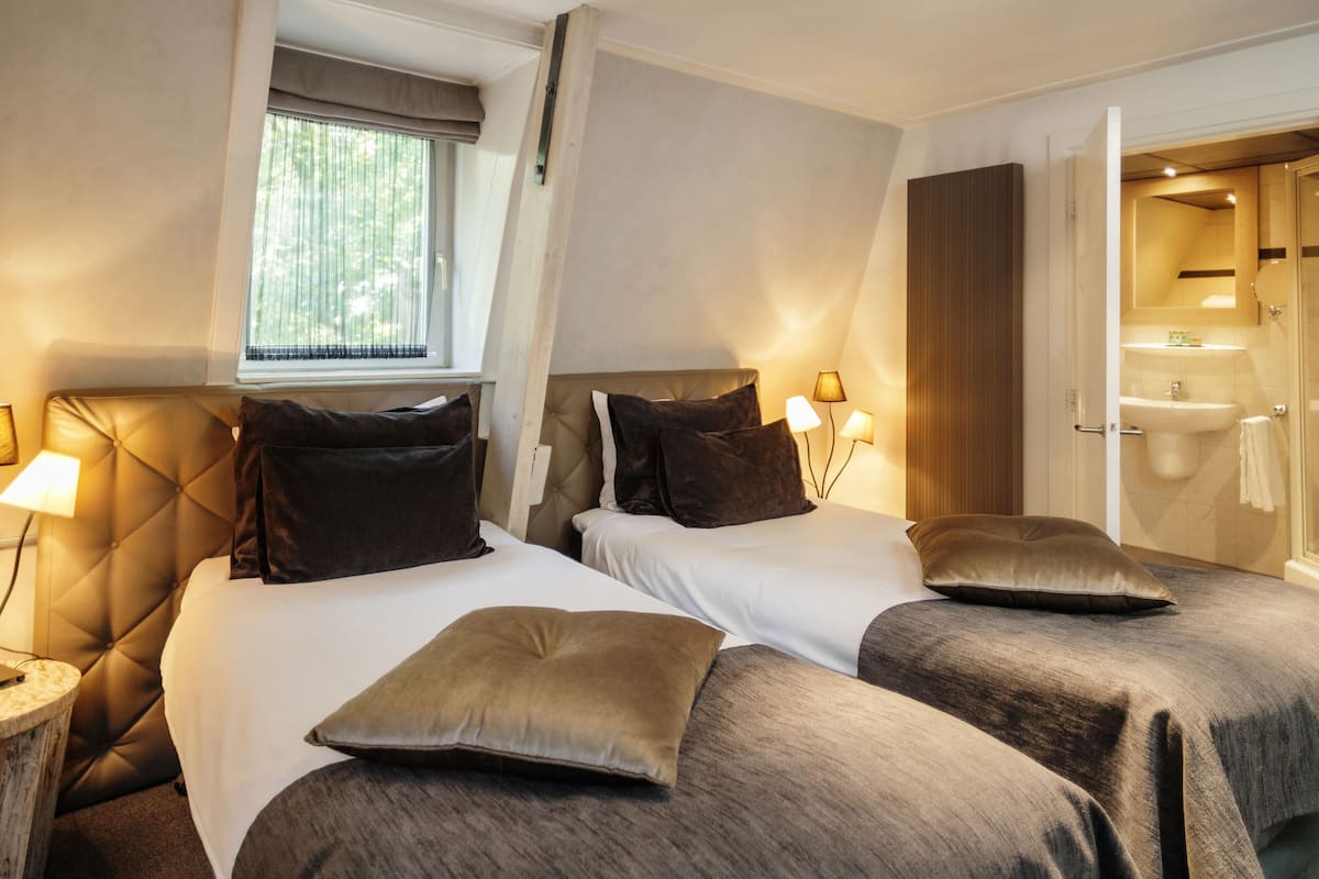 Une chambre d’hôtel avec deux lits, chacun doté d’une tête de lit, de lampes de chevet et d’une fenêtre avec des rideaux.