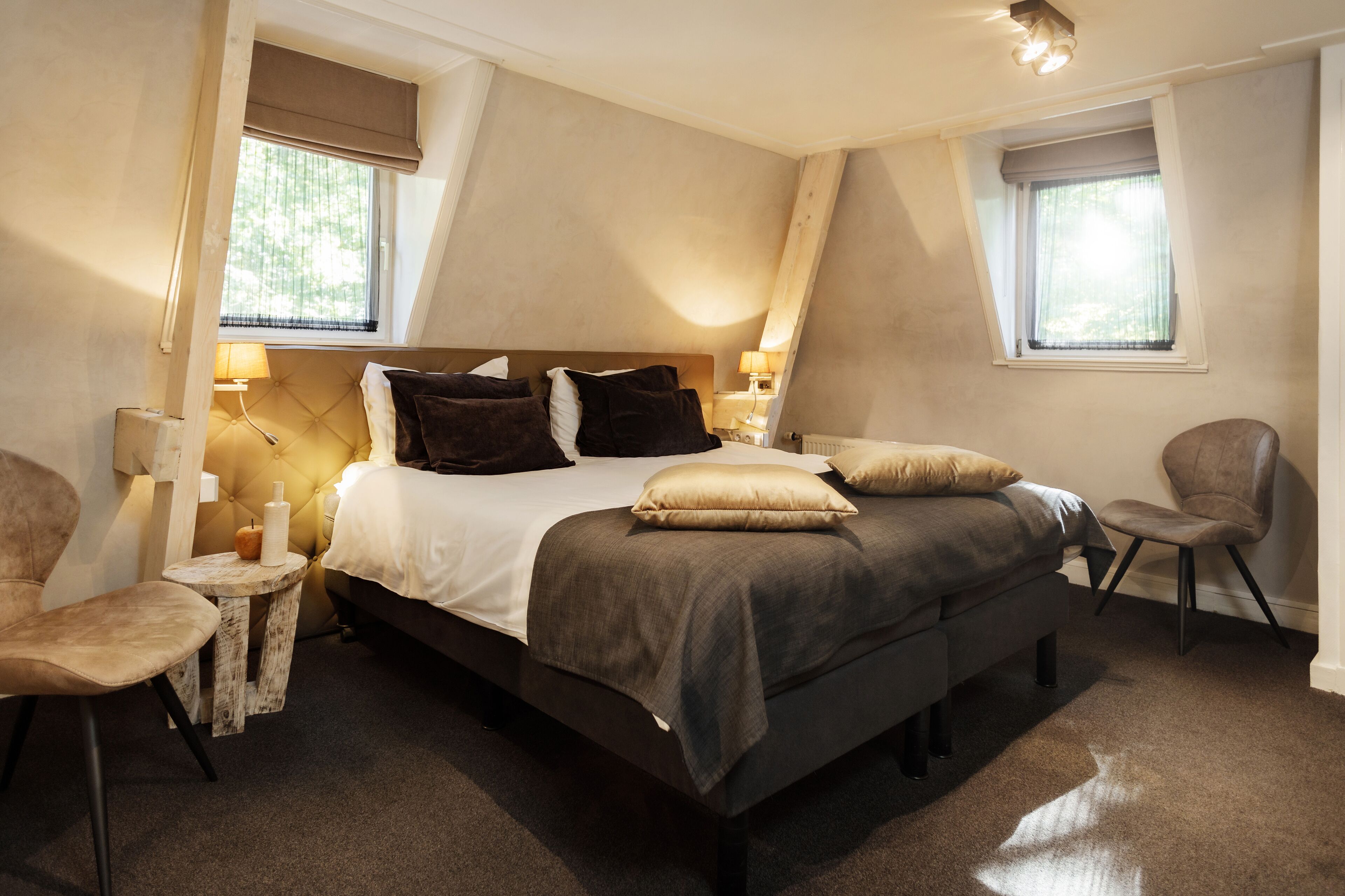 Un dormitorio con una cama, dos mesitas de noche, una silla y dos ventanas.