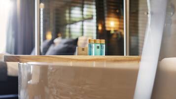 Un interior moderno con una mesa de madera, un panel de vidrio y el reflejo de una habitación con sofá y lámpara.