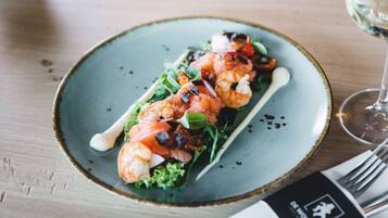 A plate of food with shrimp, vegetables, and a glass of white wine on a wooden table.