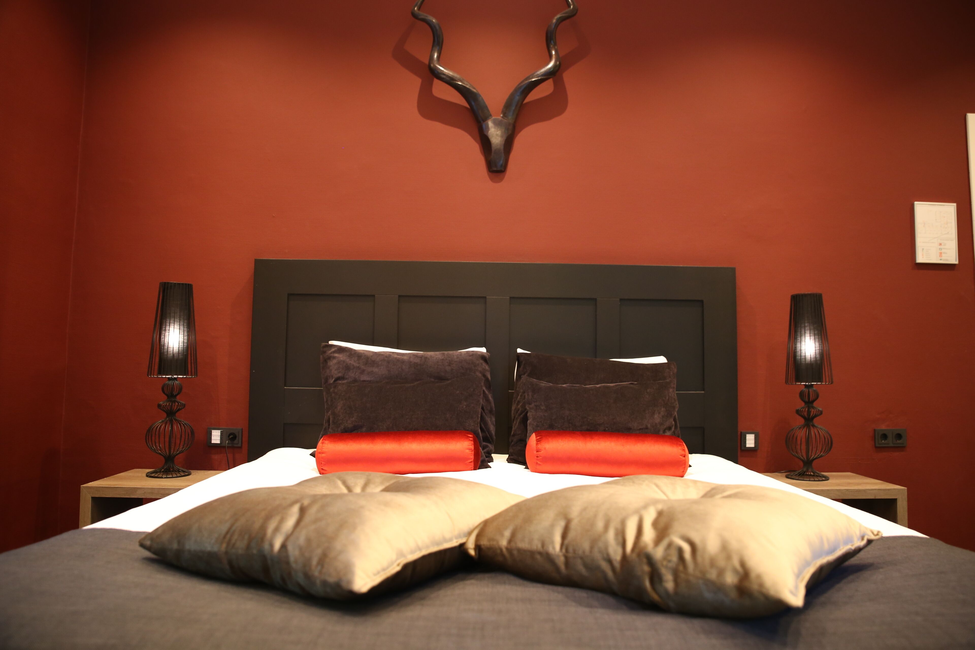A bed with two brown pillows and two orange pillows, a deer head wall decoration, and two bedside lamps.