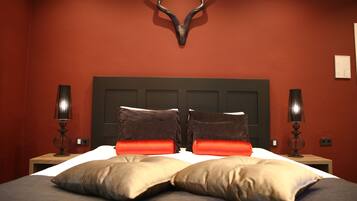 A bed with two brown pillows and two orange pillows, a deer head wall decoration, and two bedside lamps.