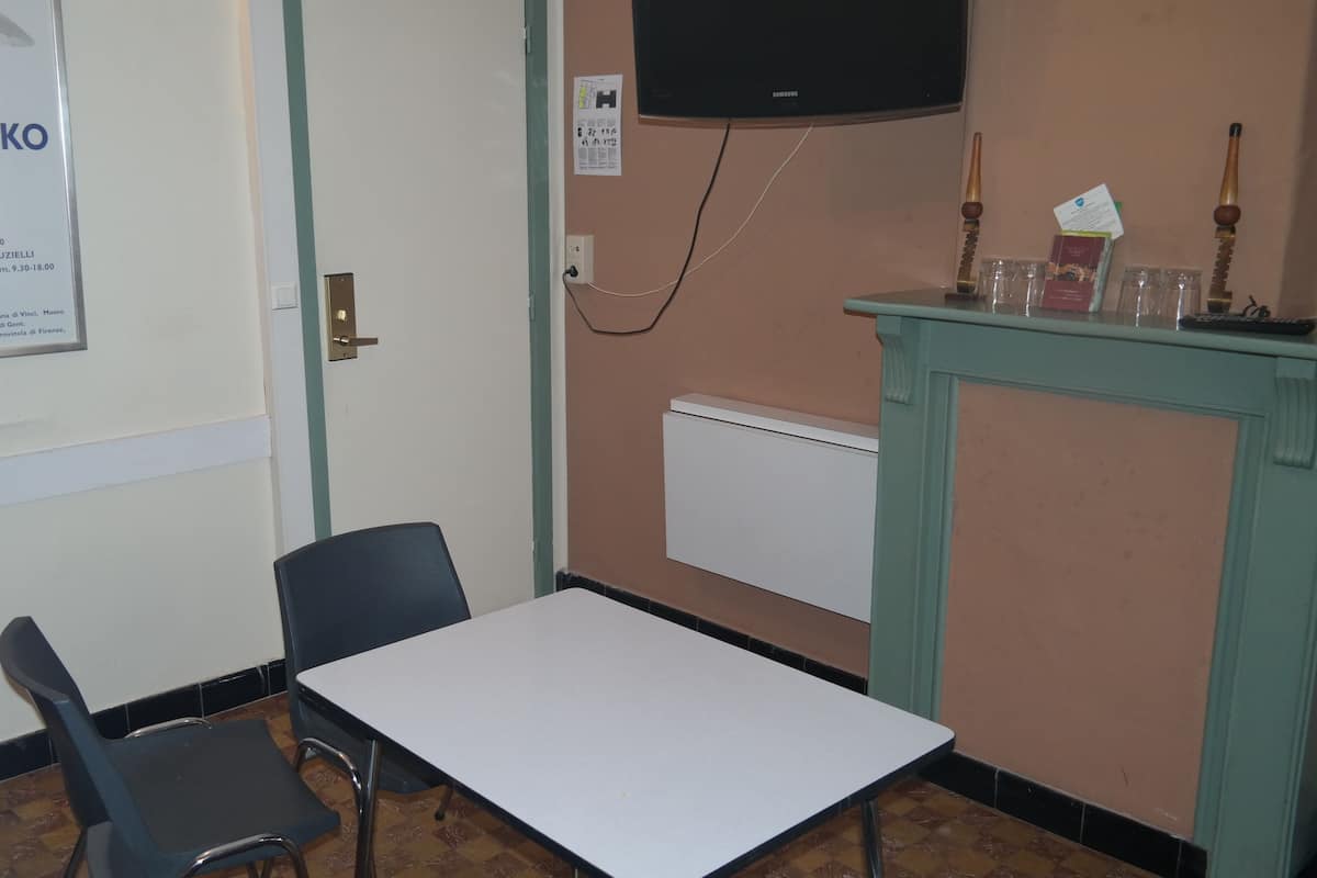 Een kamer met een witte tafel en twee stoelen, een aan de muur bevestigde televisie, en een poster op de muur.