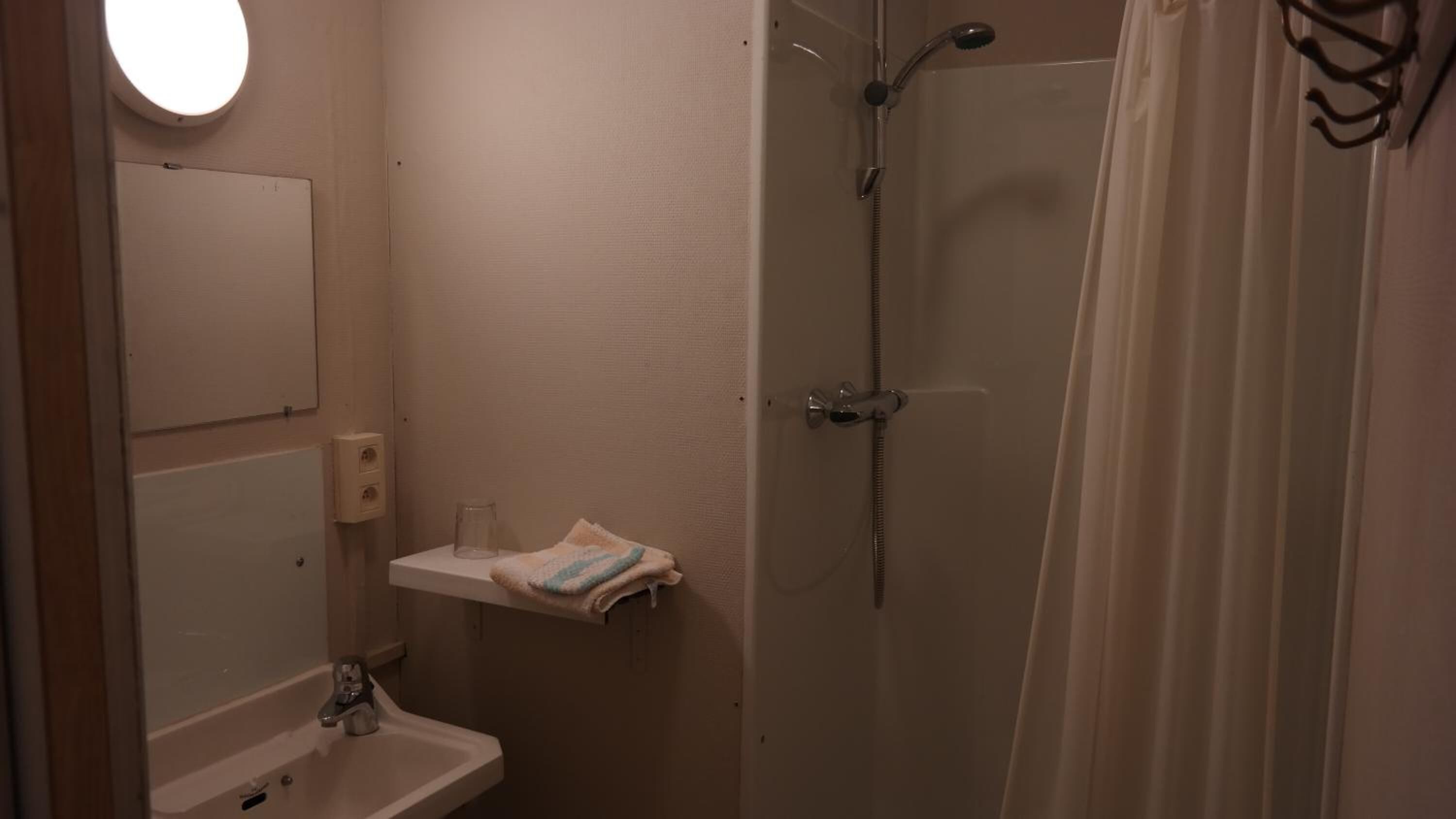 Een kleine badkamer met een wastafel, spiegel, handdoek en douche.