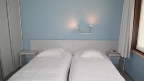 Una cama doble con ropa blanca, dos mesitas de noche y una lámpara fijada a la pared.