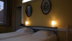 Une chambre d’hôtel avec deux lits, une table de chevet avec une lampe et deux tableaux encadrés au mur.