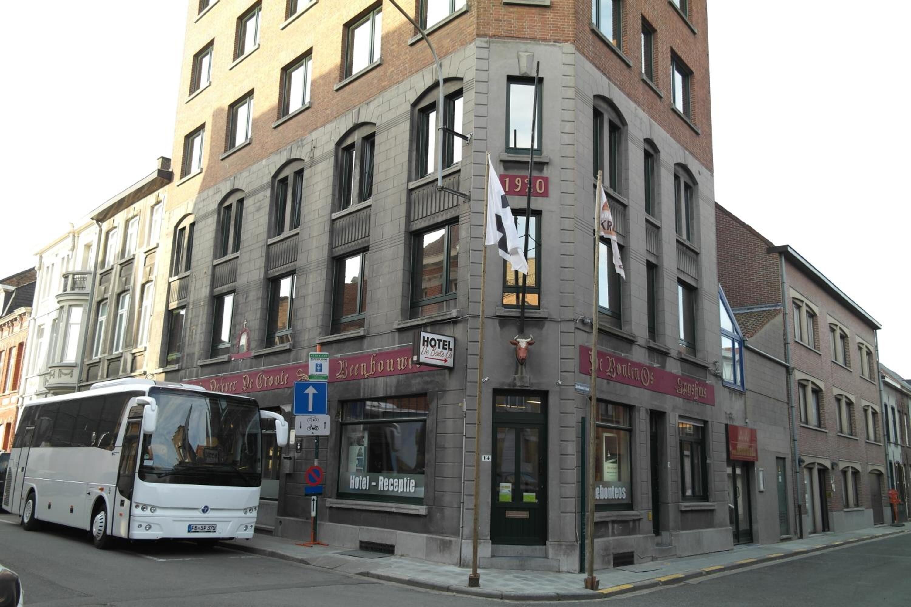Un immeuble d’angle abritant un hôtel, une réception et devant lequel est garé un autobus.
